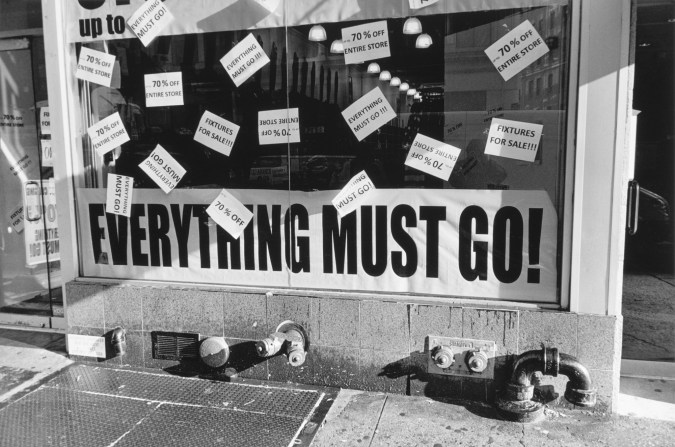 Black-and-white photograph of a storefront with all caps text everything must go!