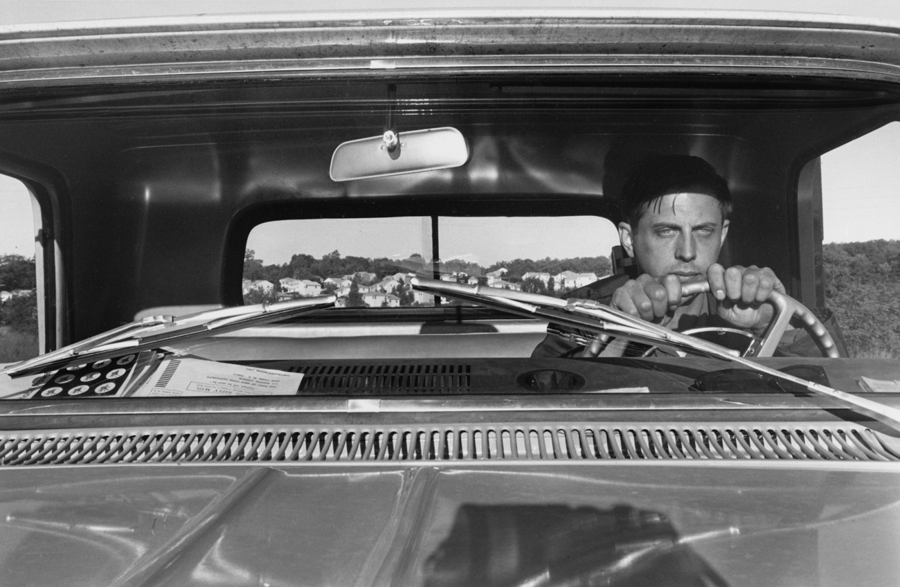 Black-and-white photograph of the artist at the wheel of a pickup truck