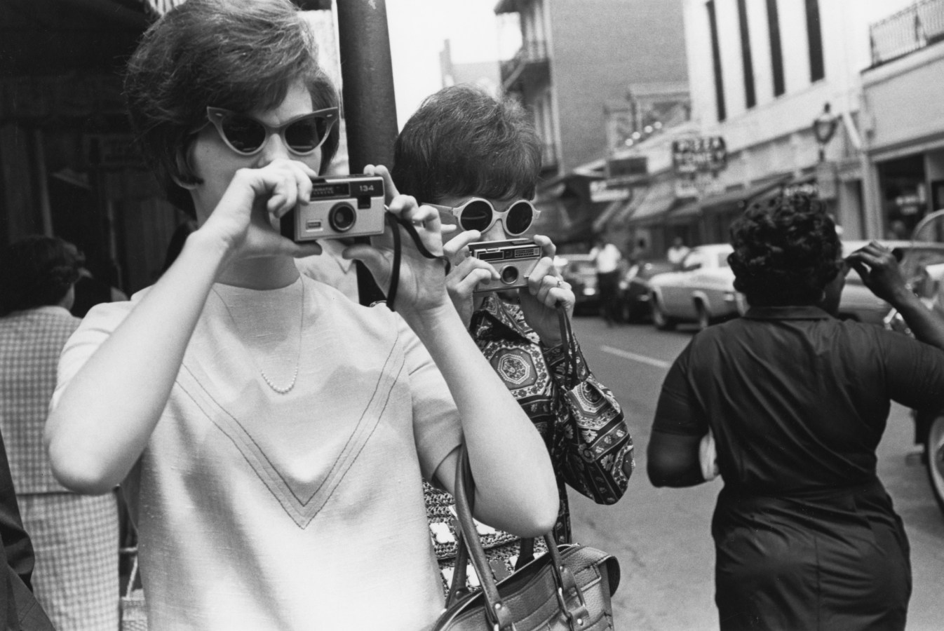 Black and white photographs of two women in sunglasses taking photographs on a city street