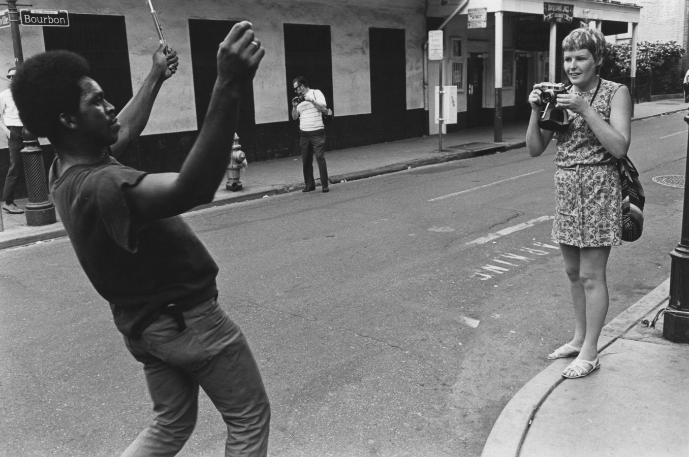 Black and white photograph of a woman taking a photograph of a man performing on a city corner