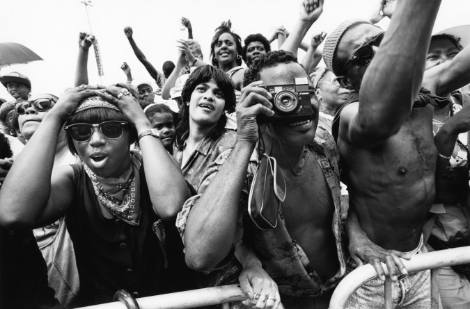 Black and white photograph of a man in a crowd holding a camera to his eye