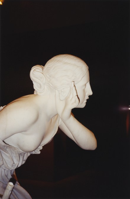 A color photograph of a marble sculpture of a woman in profile, with her hand to her ear.