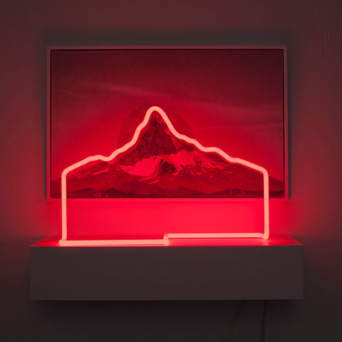 Collage of an etched print and photograph of a mountain outlined by red neon light on a shelf in front of it