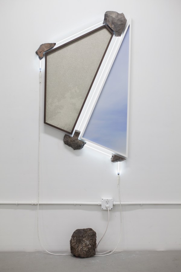 Two irregularly shaped framed prints of blank sky supported by stones and bordered by white neon lights