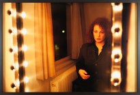Color photograph of a woman looking at her reflection in a vanity mirror