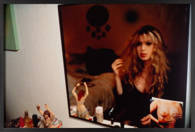 Color photograph of a figure looking in the mirror and styling their hair
