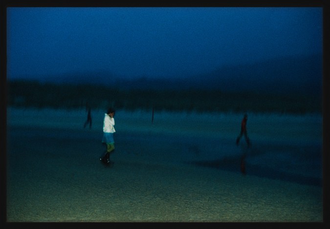 Color photograph of three figures walking along the beach framed in black