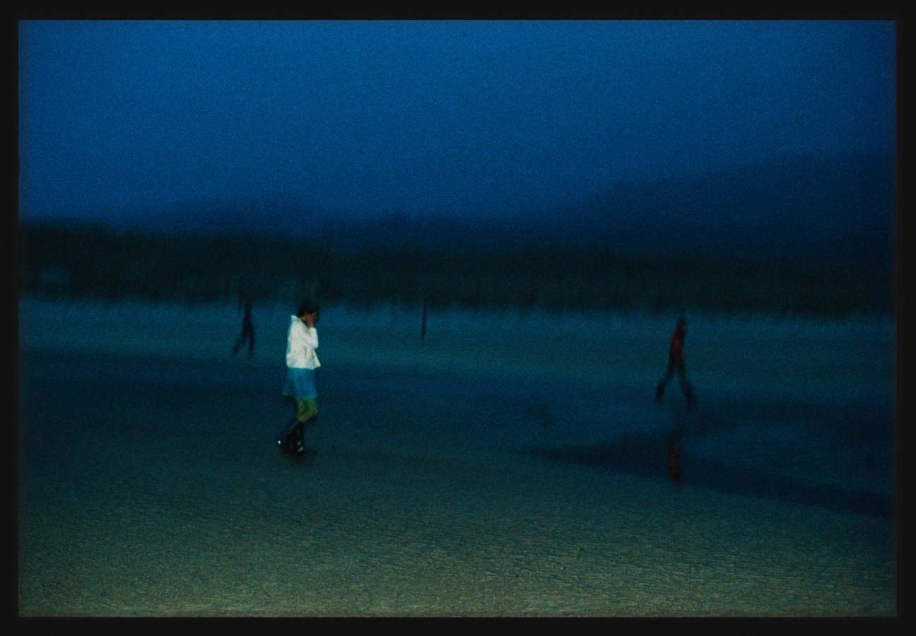 Color photograph of three figures walking along the beach framed in black