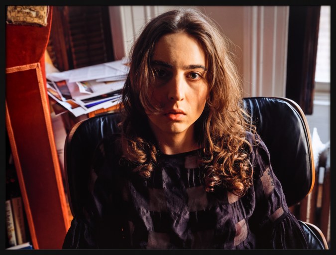 Color photograph of a seated women wearing a black lace top looking directly at camera framed in black