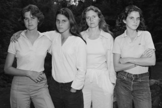 Black and white photograph of four young woman standing shoulder to shoulder in a backyard
