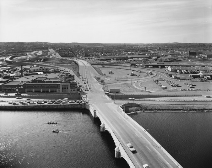 Black-and-white photograph of a highway bridge crossing a river next to a Coca-Cola plant