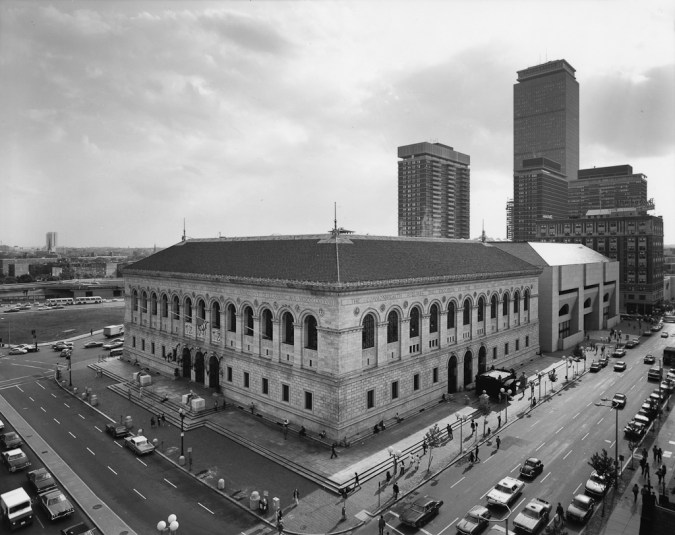 Black-and-white photograph at the corner of a low square building with rounded arch windows