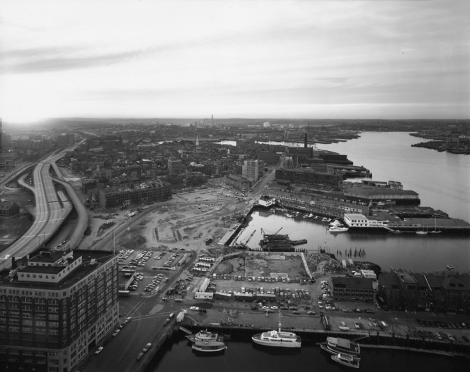 Black-and-white photograph of a low rise industrial neighborhood and a wharf on a river