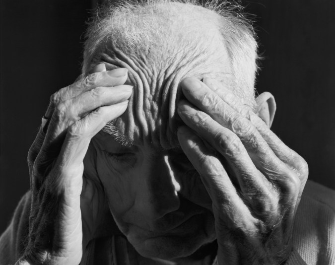 Black-and-white photograph of an old man pushing his fingers into his temples.