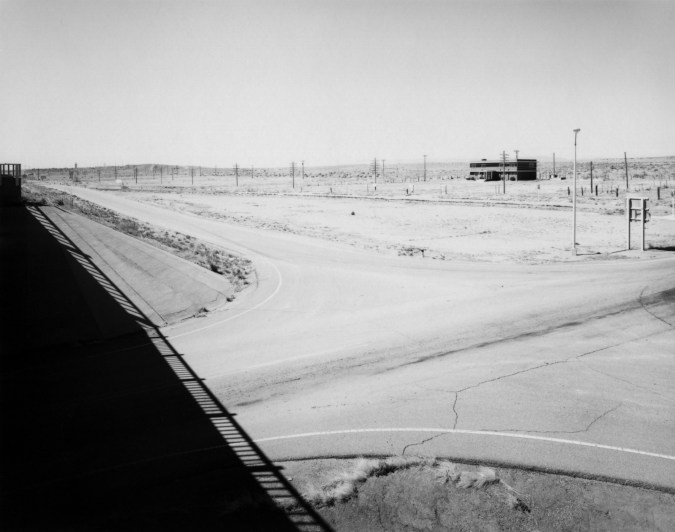 Black and white photograph of barren intersection with single building on the horizon