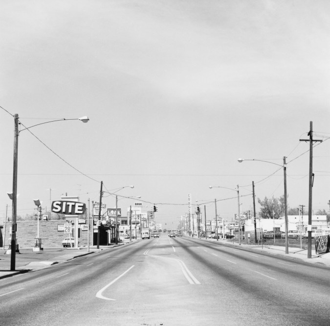 A black and white photograph of an empty street lined with businesses.
