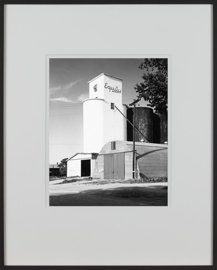 A framed vertical black and white photograph of a grain silo, with the word Equity painted at the top of the building