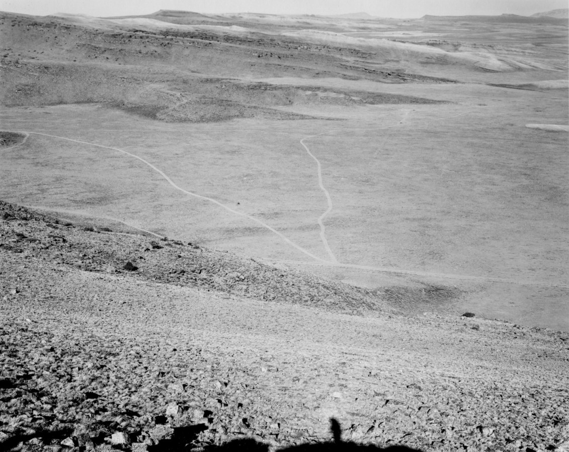 A black and white photograph of an expansive valley with roads running through it with mountains on the horizon.
