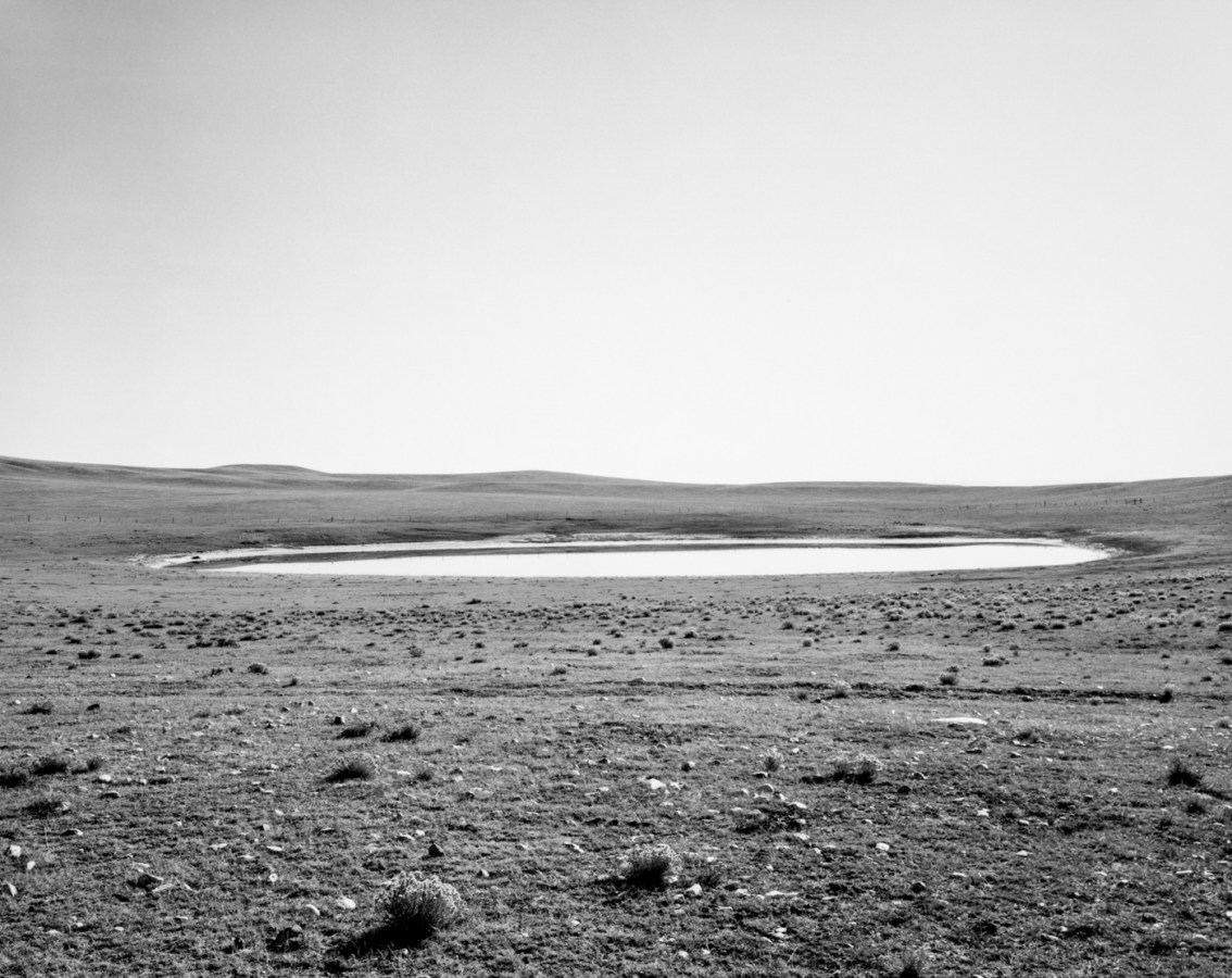 A black and white photograph of a small lake and a clear sky.