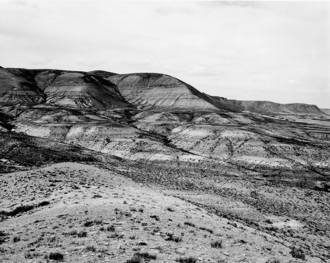 A black and white photograph with mountains and a bright cloudy sky.