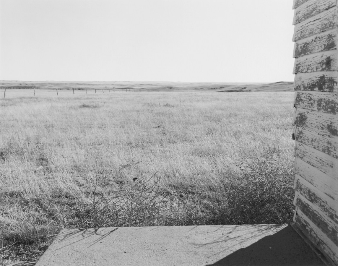 Black and white photograph of an empty plain as seen from the porch of an abandoned school