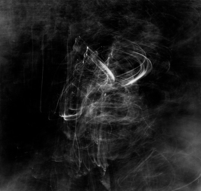 Square black-and-white long-exposure photograph of faint squiggly light trails on moving water