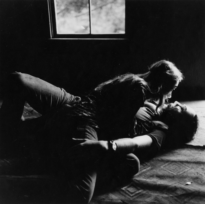 Black-and-white photograph of a couple in masks laying on the floor in embrace