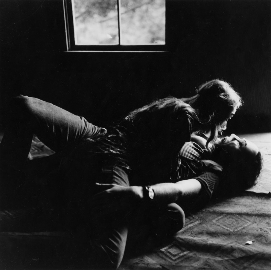 Black-and-white photograph of a couple in masks laying on the floor in embrace