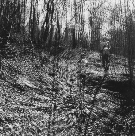 Black and white photograph of two figures making their way up a forested hill