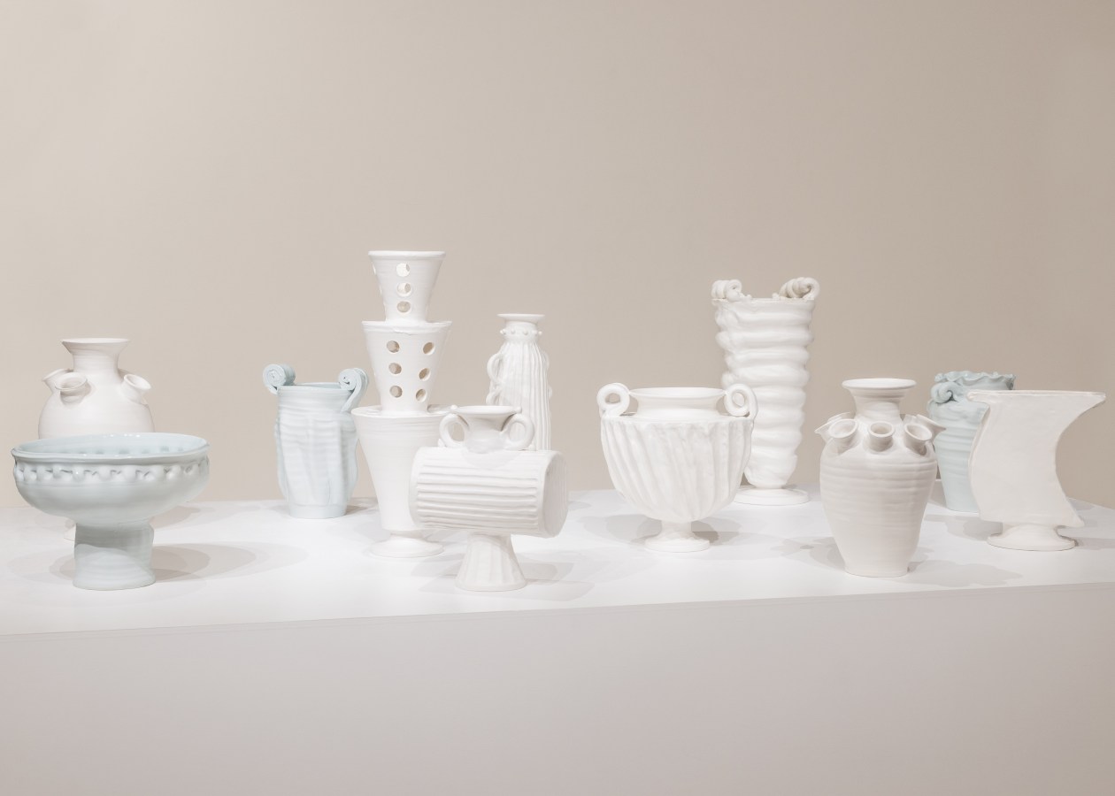 Color photograph of several ceramic vases on a white pedestal against a white wall