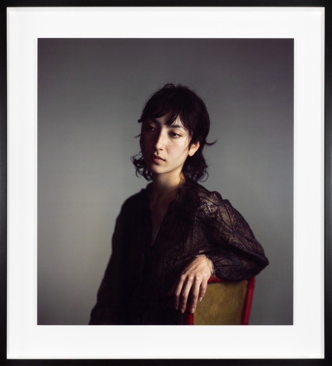 Color photograph of a seated figure in a black lace top framed in black