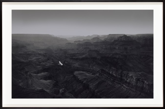 Black and white photograph of a desert canyon with a small river running through the center framed in black