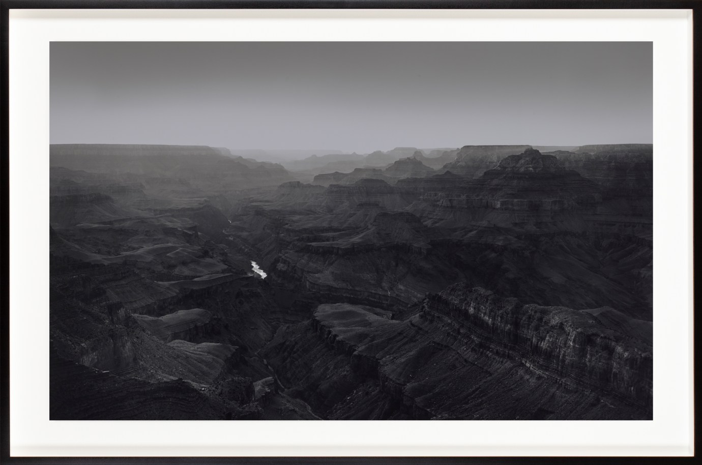 Black and white photograph of a desert canyon with a small river running through the center framed in black