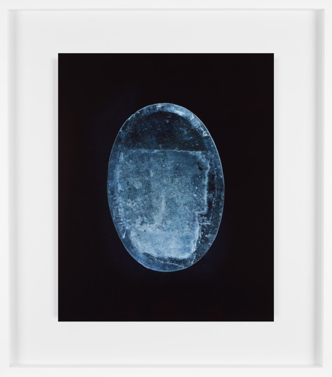 Color photograph of an oval blueish mirror with dust and streaks