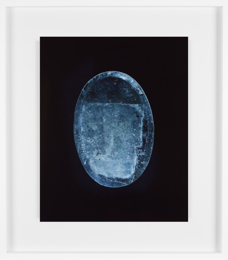 Color photograph of an oval blueish mirror with dust and streaks