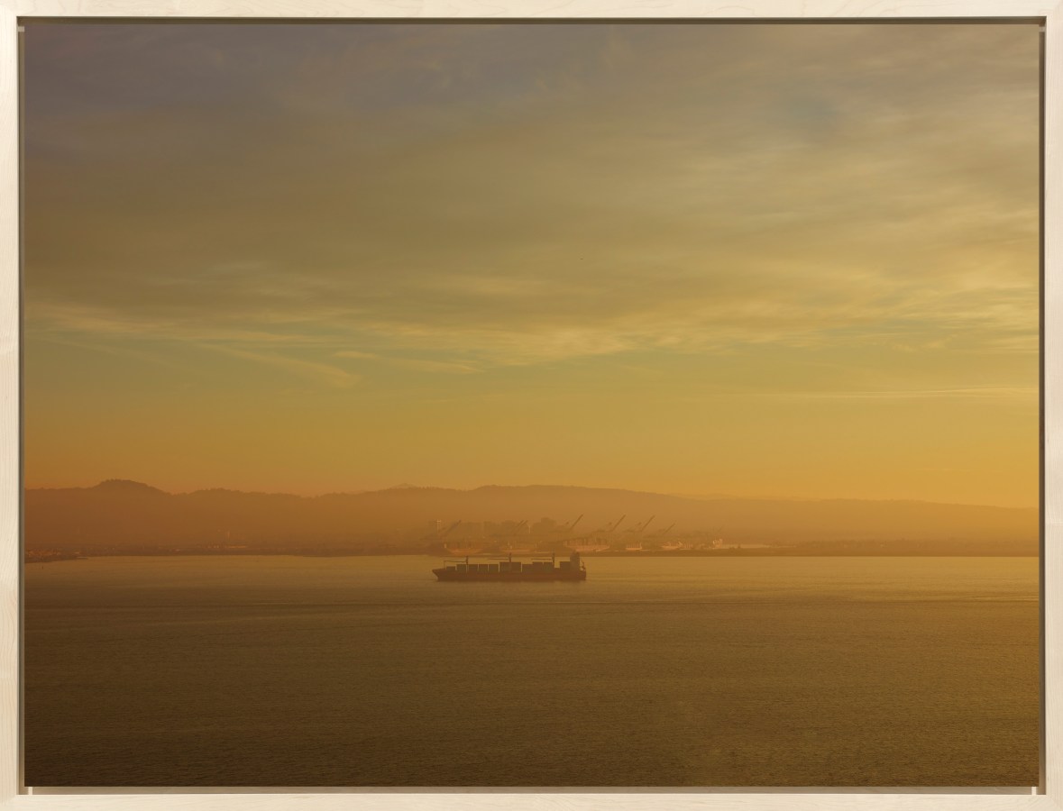 Color image of a color photograph of a cargo ship on the water during a hazy morning framed in bleached wood