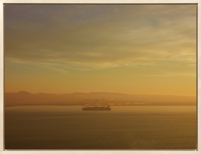 Color image of a color photograph of a cargo ship on the water during a hazy morning framed in bleached wood