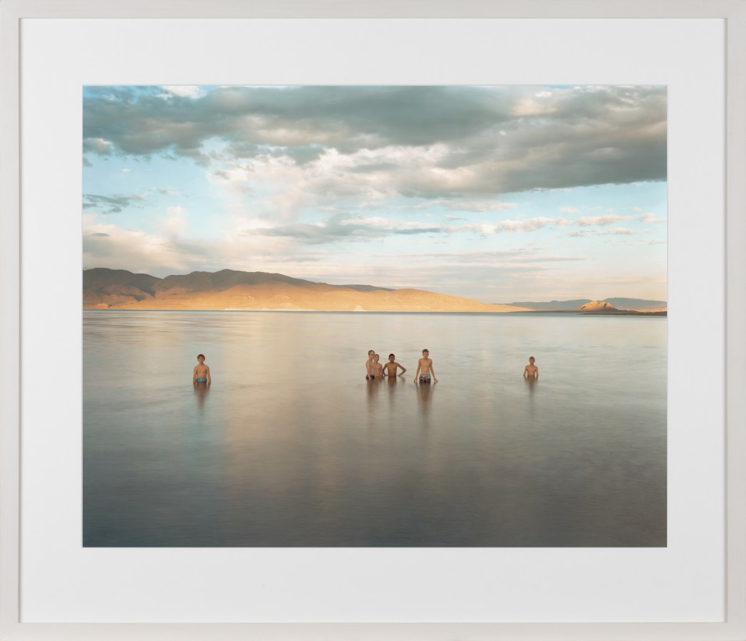 Color image of a color photograph of several figures waist deep in lake in middle of desert framed in white