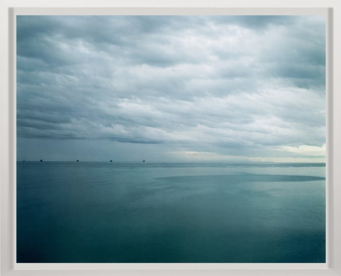 Color photograph of oil derricks off the coast of Santa Barbara on a cloudy day framed in white