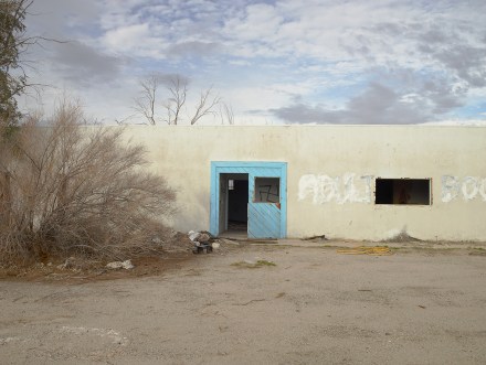 Color photograph of an abandoned building with grafitti of a swastika visible through a broken door