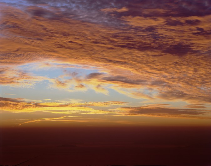Color photograph of San Francisco Bay and Golden Gate Bridge during sunrise on a cloudy and foggy morning