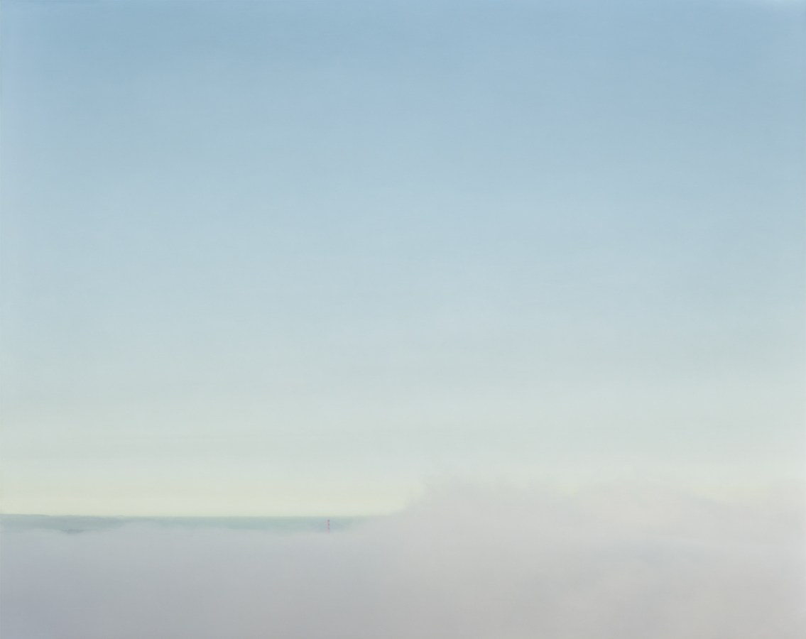 Color photograph of the Golden Gate Bridge on the horizon almost completely obscured by low-lying fog under a clear pale blue sky