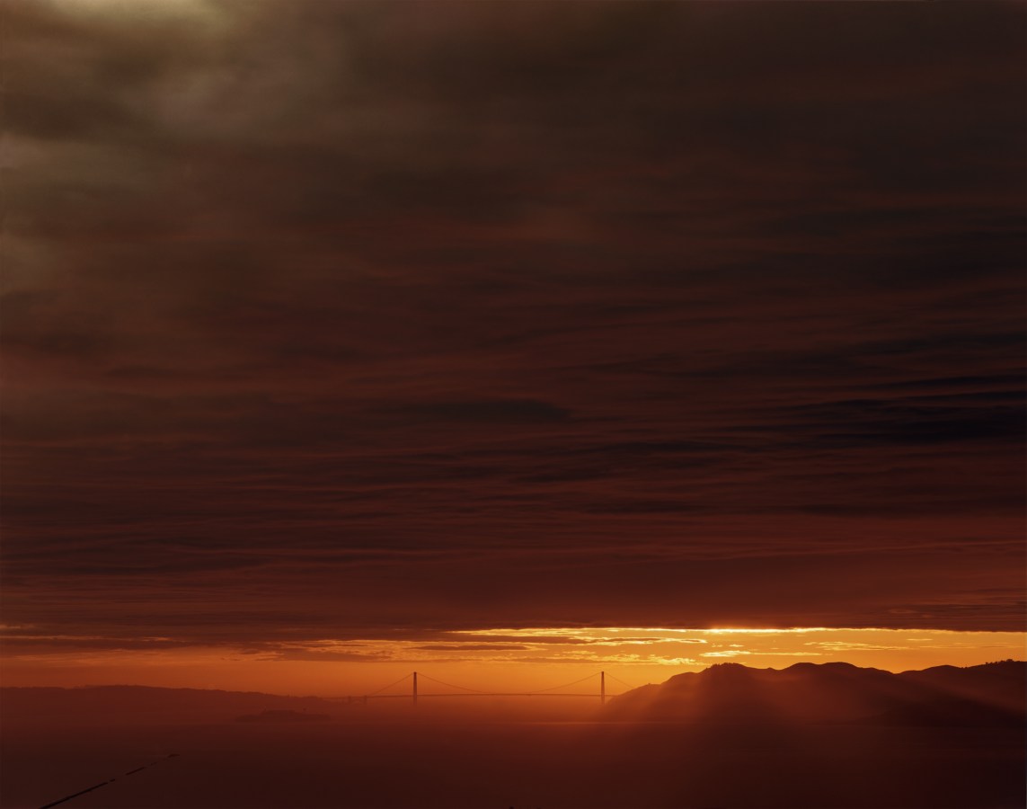 Color photograph of San Francisco Bay and Golden Gate Bridge during sunset with thick dark clouds