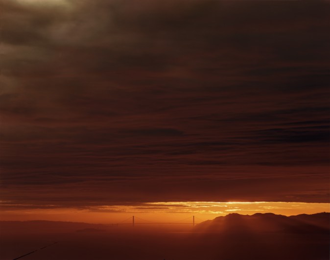 Color photograph of San Francisco Bay and Golden Gate Bridge during sunset with thick dark clouds