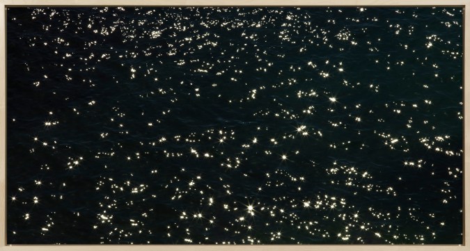 Color photograph of ocean water being reflected by the sun framed in bleached wood frame