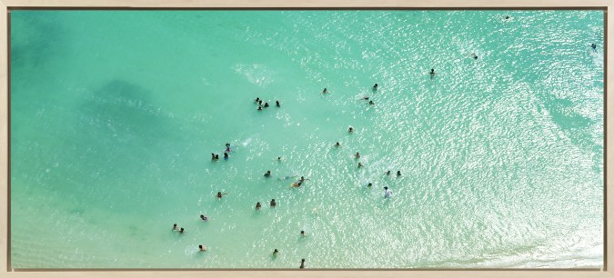 Color aerial photograph of scattered swimmers in a shallow blue-green sea near the shore