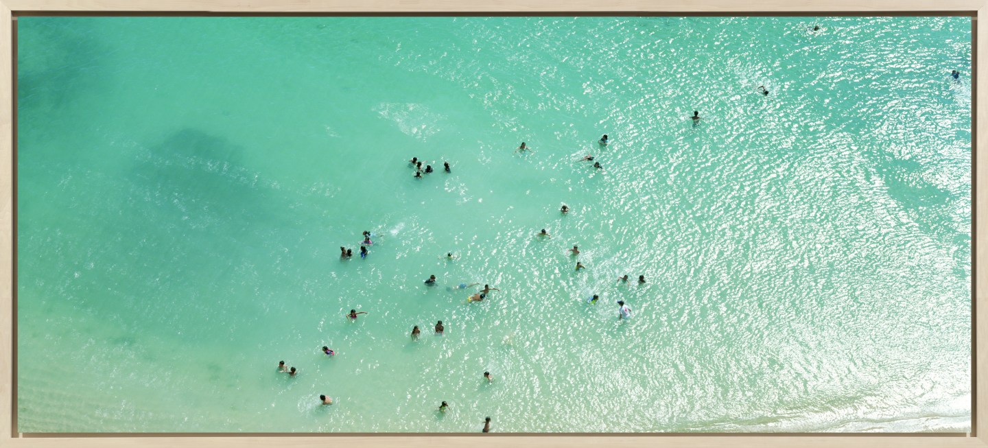 Color aerial photograph of scattered swimmers in a shallow blue-green sea near the shore