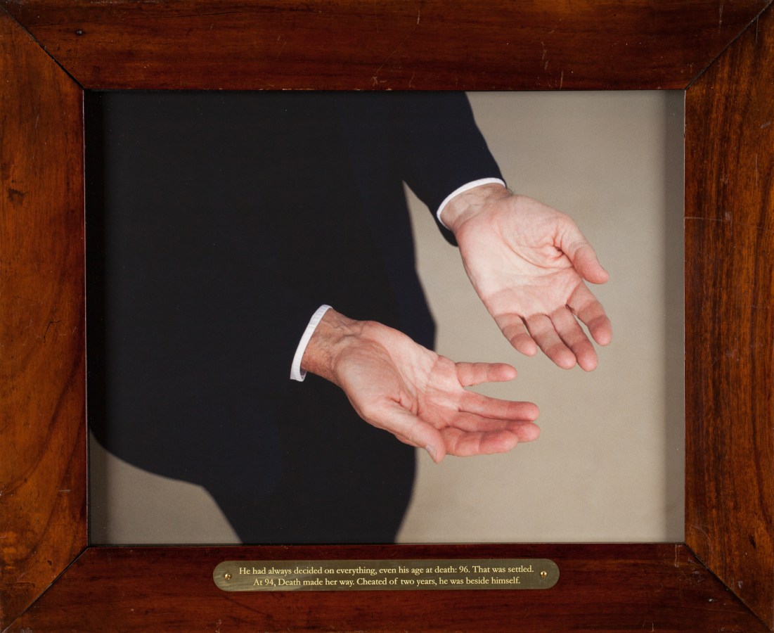 Color photograph of a mans up turned palms in wooden frame with plaque