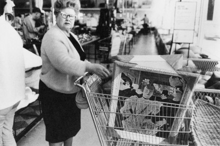Black and white photograph of a woman with several framed paintings in a shopping cart