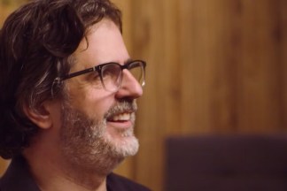 A color video still of a man wearing glasses, smiling in profile